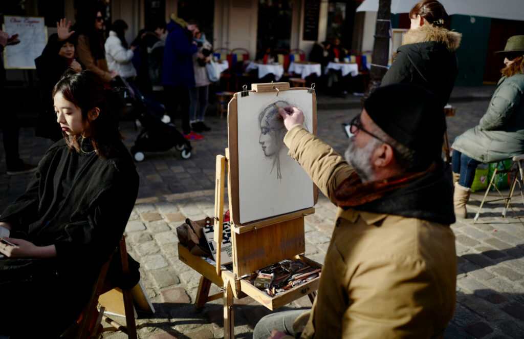 Artist doing a portrait of a tourist at Place du Tertre in Montmartre, Paris